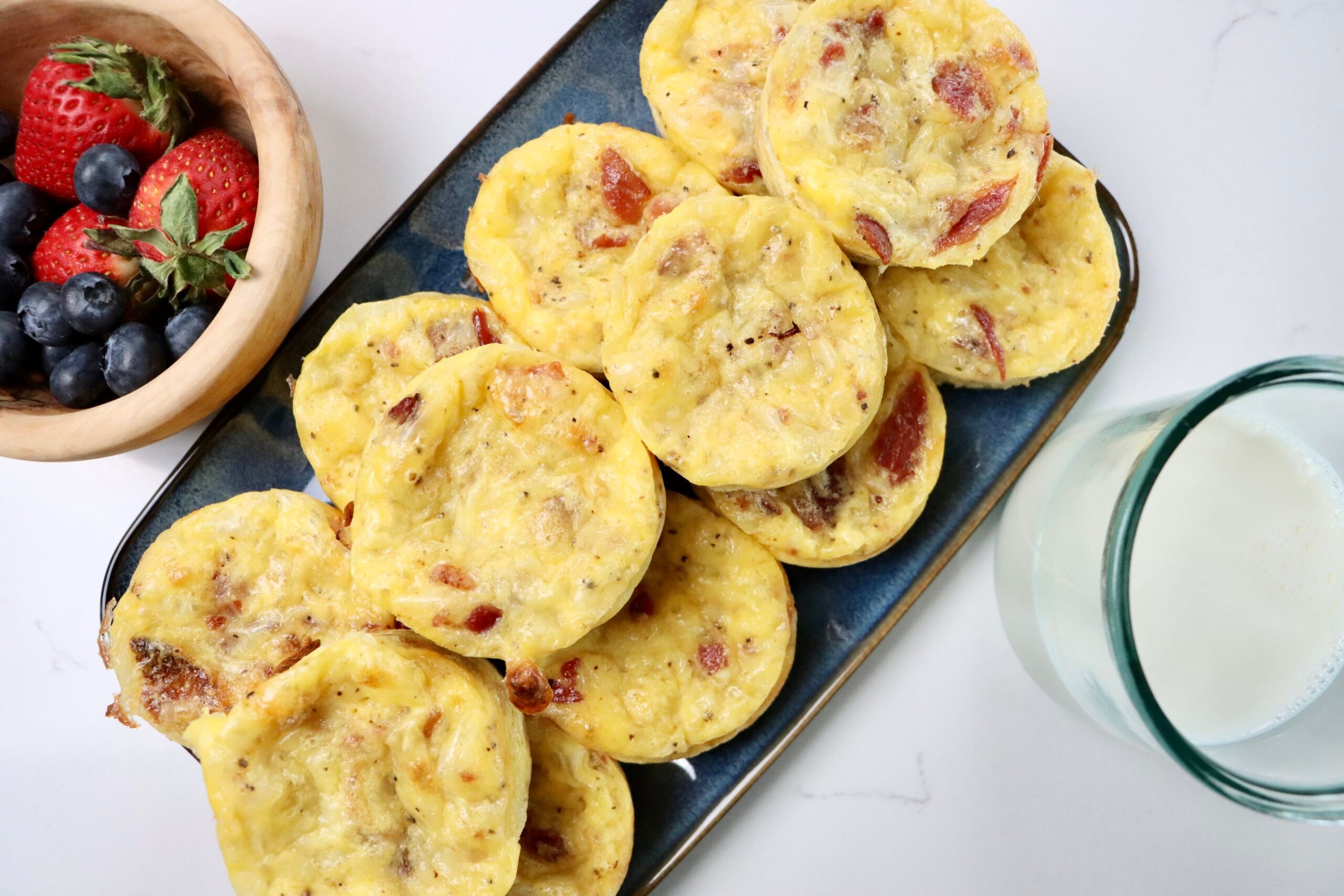 Bacon, egg and cheese muffins next to a bowl of berries and a small glass of milk