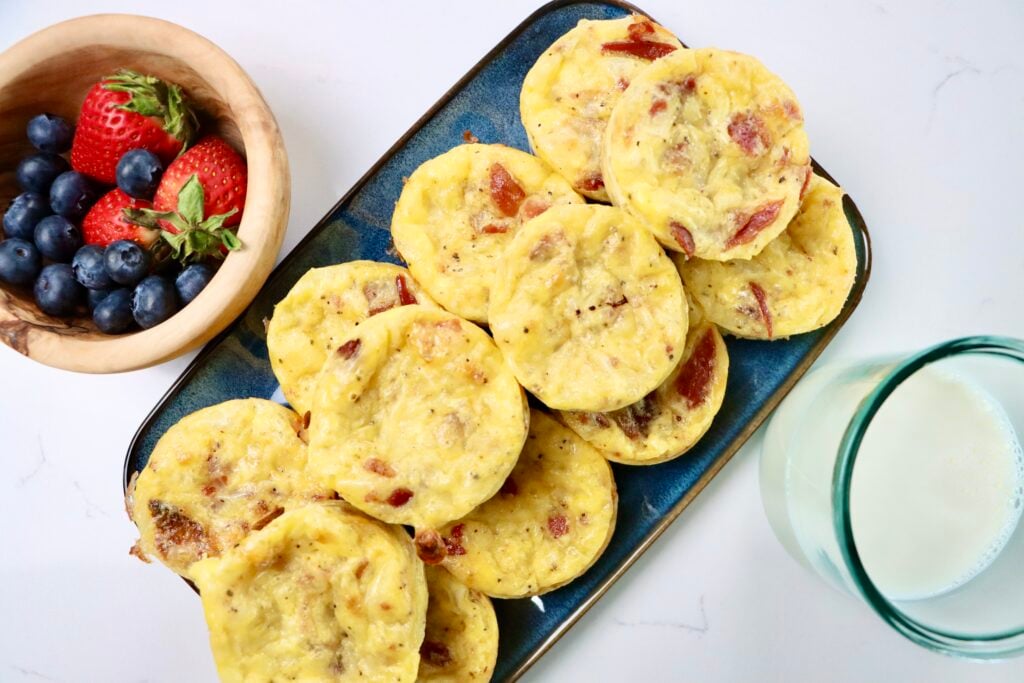 Bacon, egg and cheese muffins next to a bowl of berries and a small glass of milk