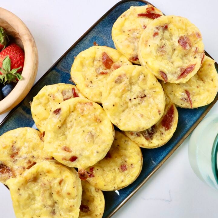 Bacon, egg and cheese muffins next to a bowl of berries and a small glass of milk