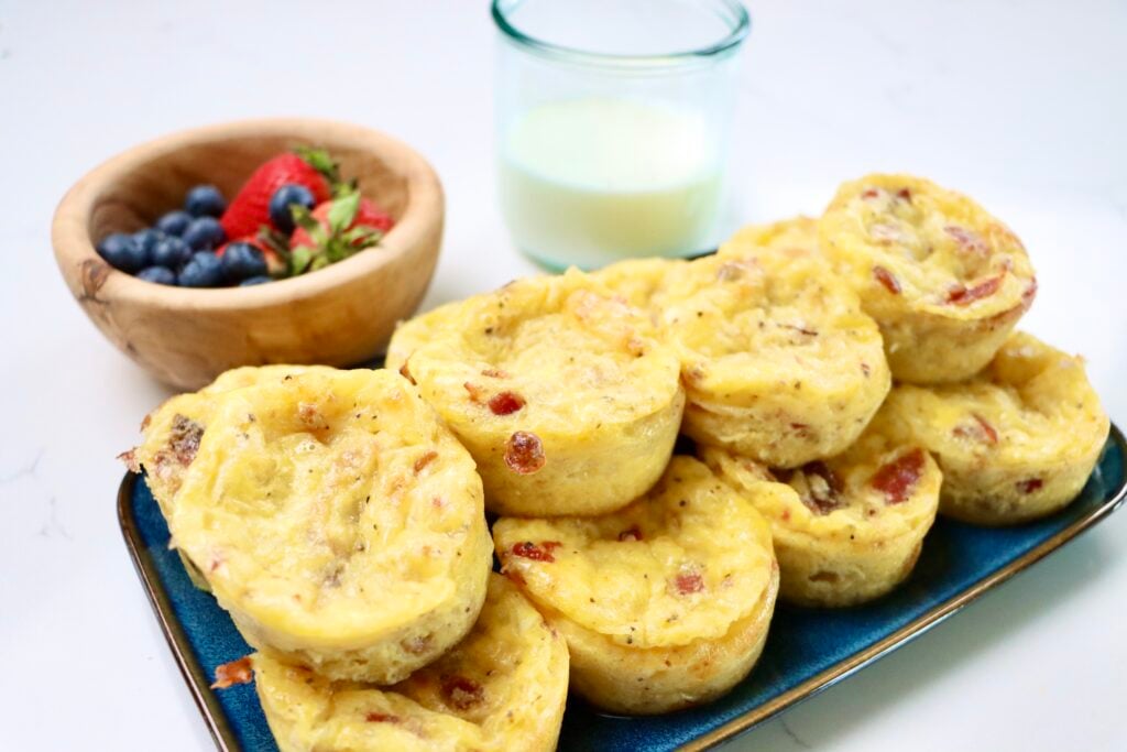 Bacon, egg and cheese muffins next to a bowl of berries and a small glass of milk