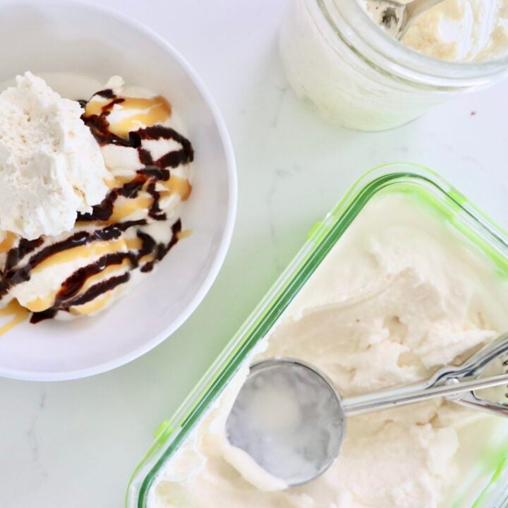 Homemade Vanilla Ice cream in a bowl with chocolate and caramel sauce topped with whipped cream next to a container of vanilla ice cream