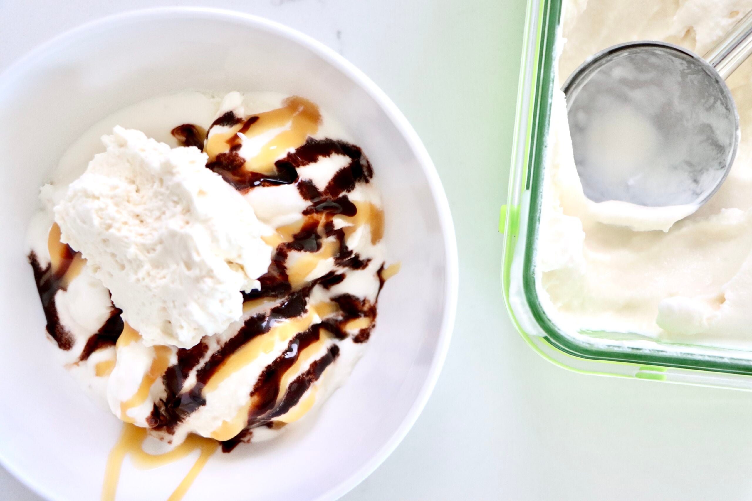 Homemade Vanilla Ice cream in a bowl with chocolate and caramel sauce topped with whipped cream next to a container of vanilla ice cream