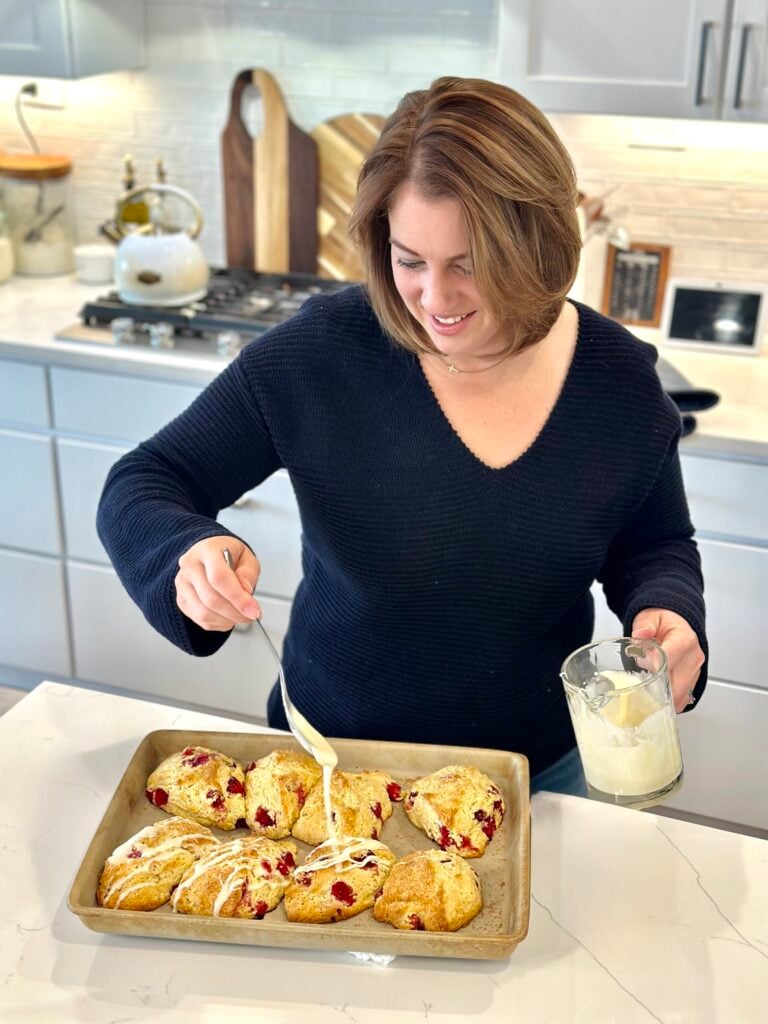 Woman in the kitchen putting glaze on cranberry orange scones