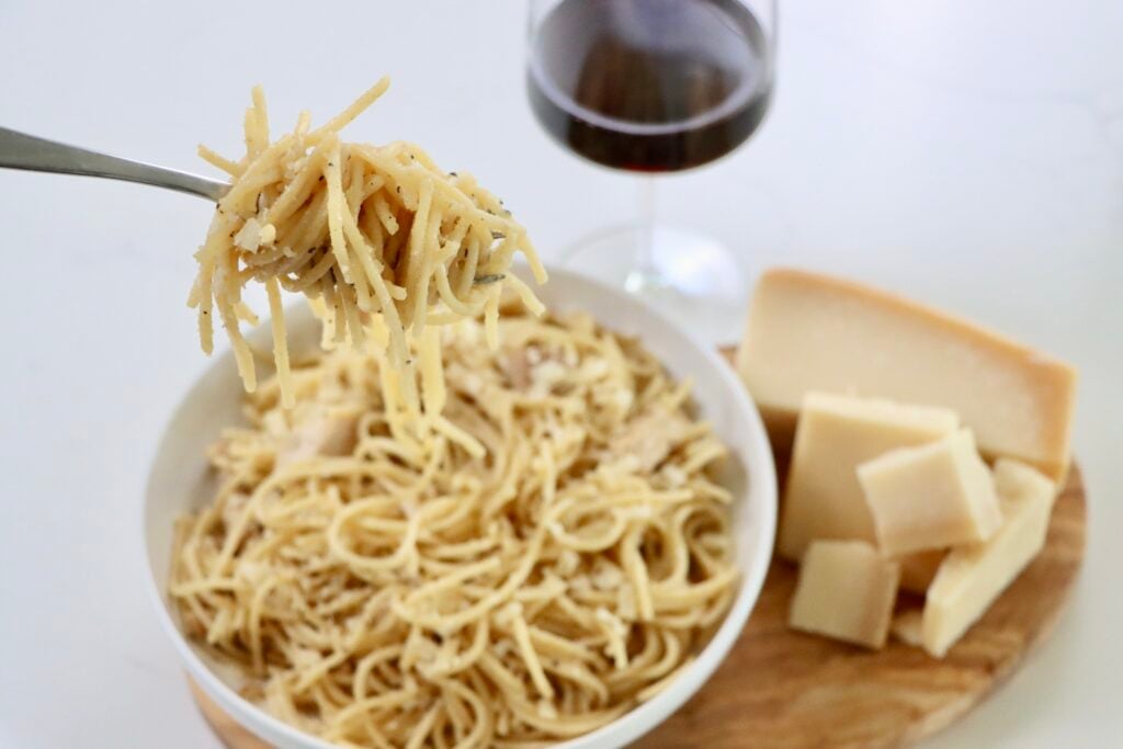 Chicken spaghetti in a bowl on a cutting board with parmesan cheese and a glass of wine