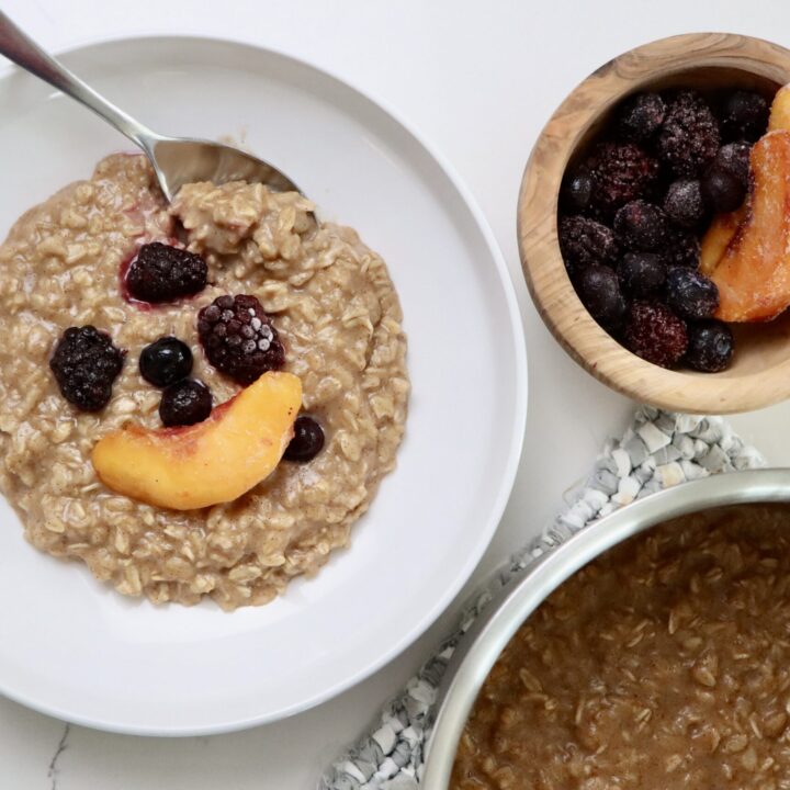 Maple Cinnamon Oatmeal in a bowl with fruit on top and a bowl of fruit and a pot of oatmeal on a hot pad