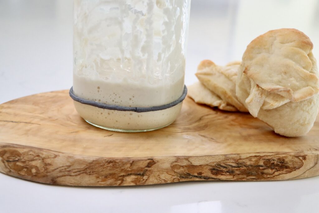 A jar with sourdough starter on a cutting board with sourdough biscuits