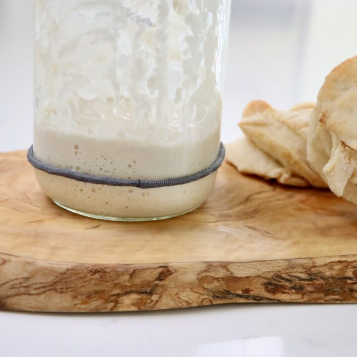 A jar with sourdough starter on a cutting board with sourdough biscuits