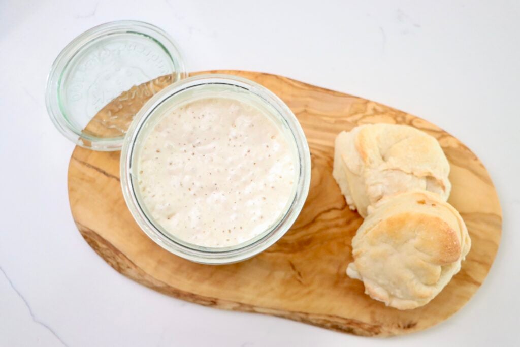 A jar with sourdough starter on a cutting board with sourdough biscuits