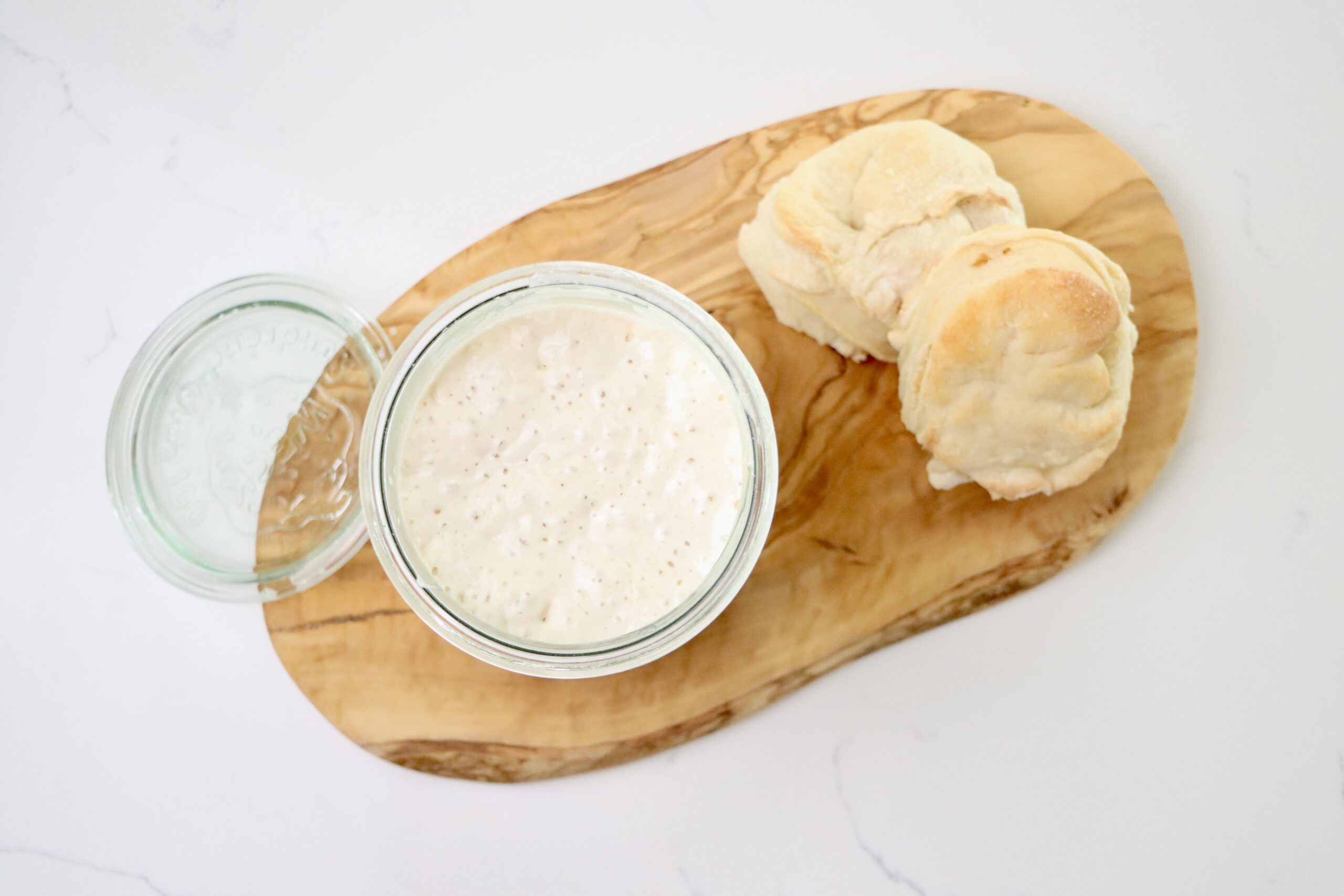 A jar with sourdough starter on a cutting board with sourdough biscuits