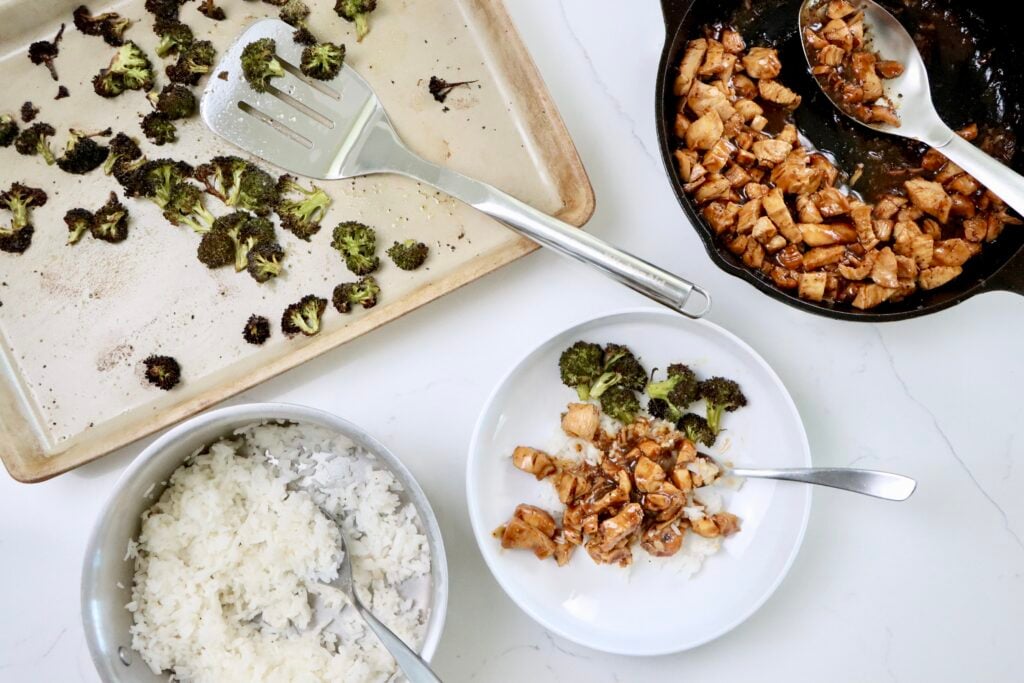 Teriyaki Chicken with Jasmine Rice and Roasted Broccoli in a white bowl with a pan of broccoli, teriyaki chicken and rice