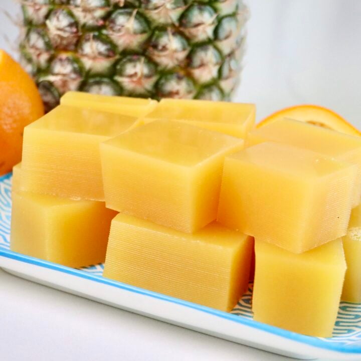 Pineapple Orange Gummies on a plate with a whole pineapple and a sliced orange for garnish