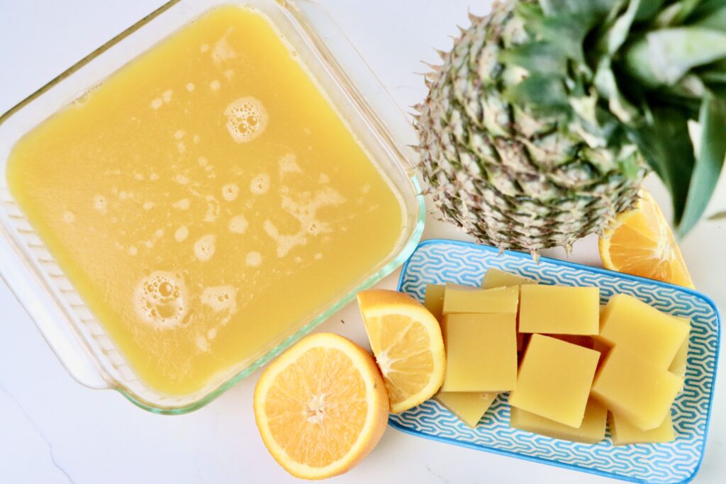 Pineapple Orange Gummies on a plate with a whole pineapple and a sliced orange for garnish