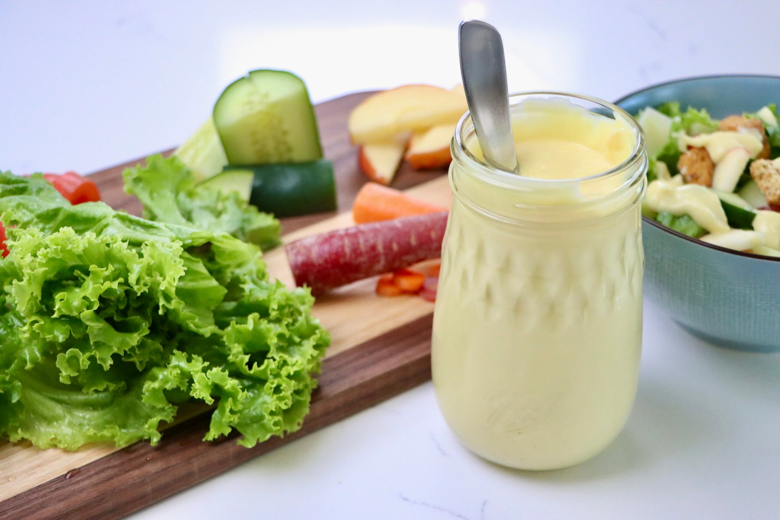 Salad Dressing without oil in a jar next to a bowl of salad and salad fixings on a cutting board