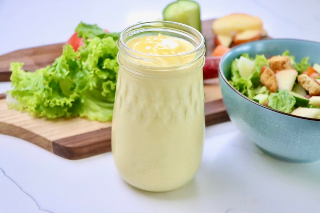 Salad Dressing without oil in a jar next to a bowl of salad and salad fixings on a cutting board