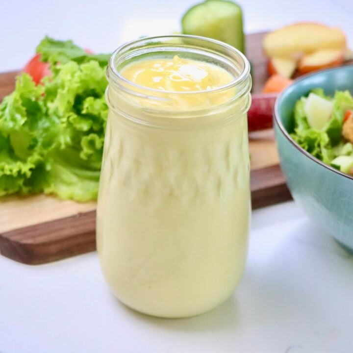 Salad Dressing without oil in a jar next to a bowl of salad and salad fixings on a cutting board