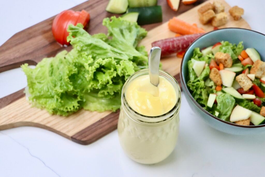 Salad Dressing without oil in a jar next to a bowl of salad and salad fixings on a cutting board