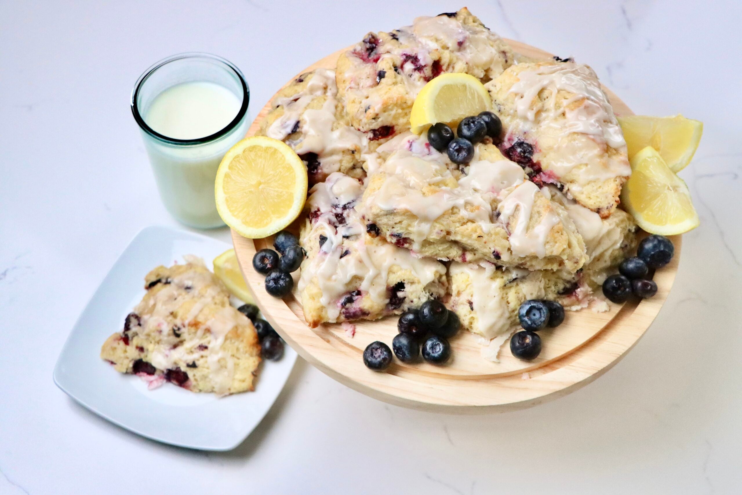 Sourdough Blueberry Lemon Scones on a tray with lemons and blueberries and a glass of milk