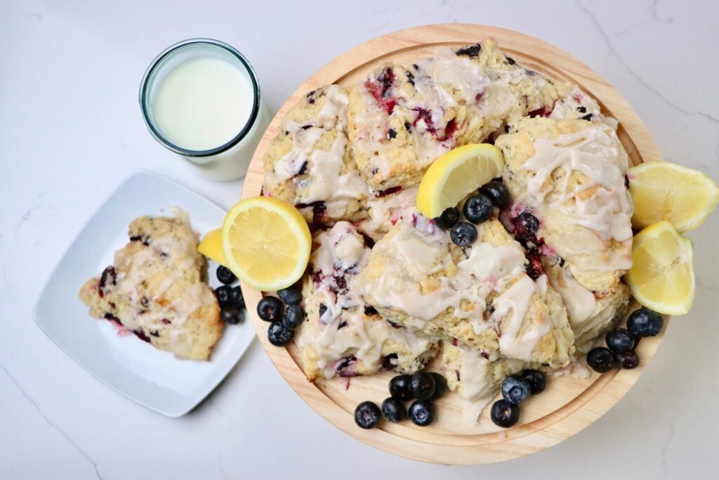 Sourdough Blueberry Lemon Scones on a tray with lemons and blueberries and a glass of milk