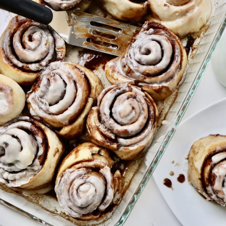 Sourdough Cinnamon Rolls in a pan with one cinnamon roll on a plate sitting next to a bowl of berries and a glass of milk.