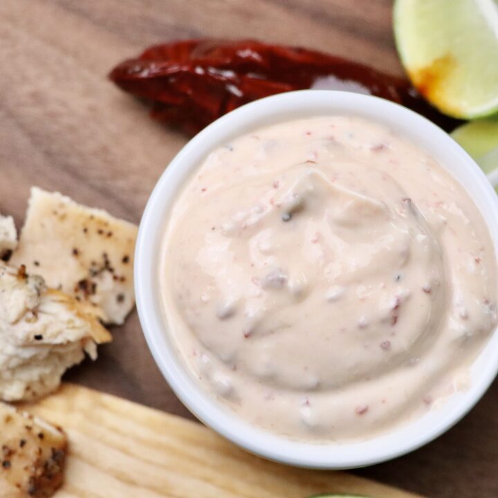 Chipotle Crema with Limes and a Chipotle Pepper on a cutting board with grilled chicken