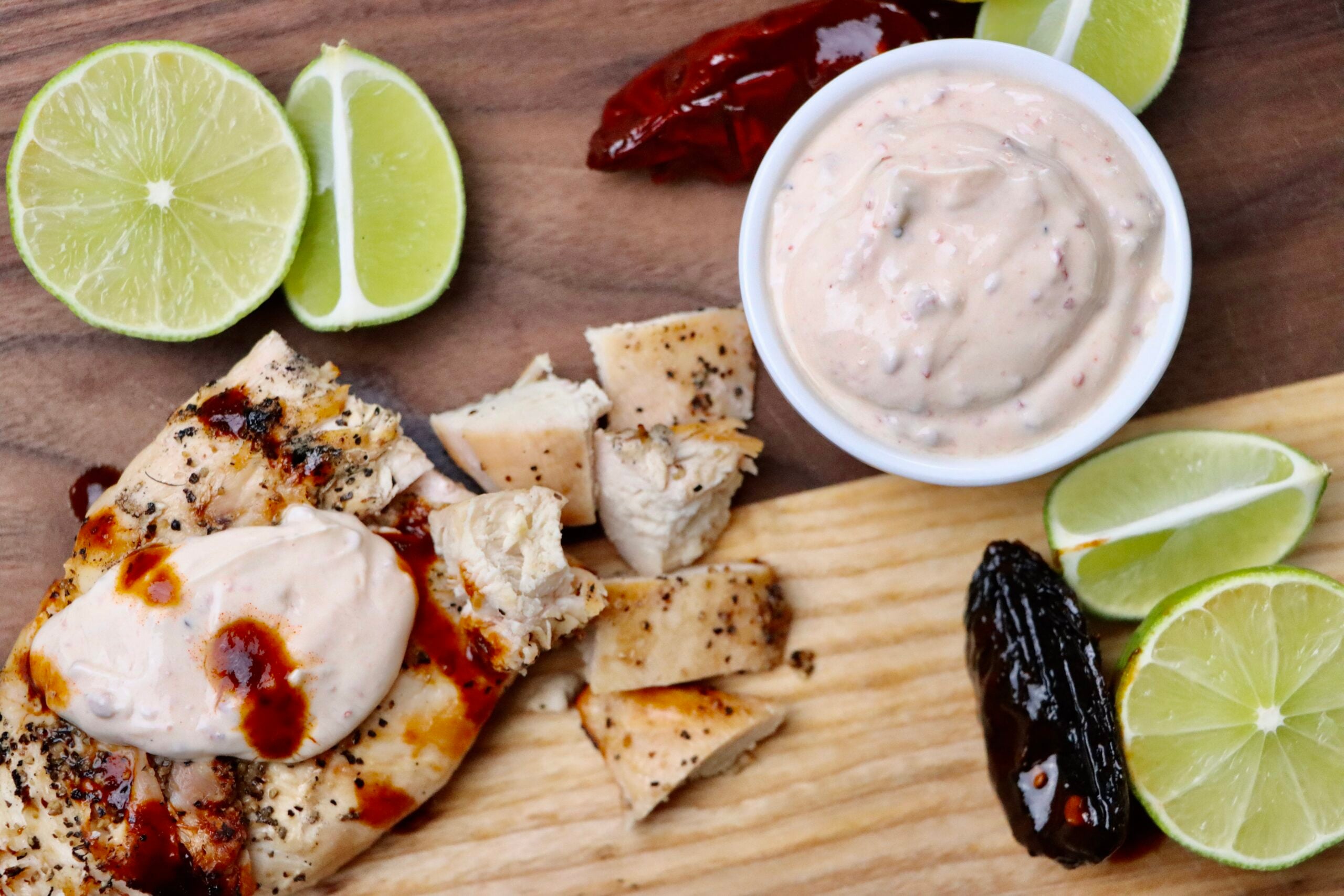 Chipotle Crema with Limes and a Chipotle Pepper on a cutting board with grilled chicken
