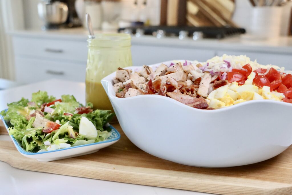 Homemade Cobb Salad in a bowl and a plate next to homemade honey mustard dressing