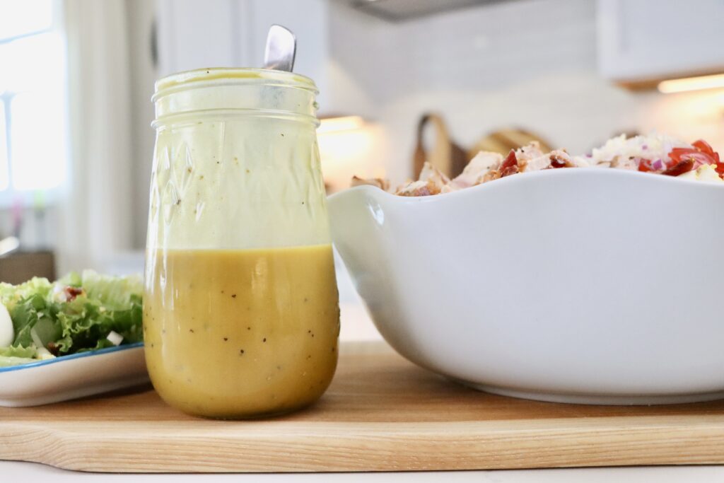 Homemade Honey Mustard Dressing in a jar next to a bowl and plate of cobb salad.