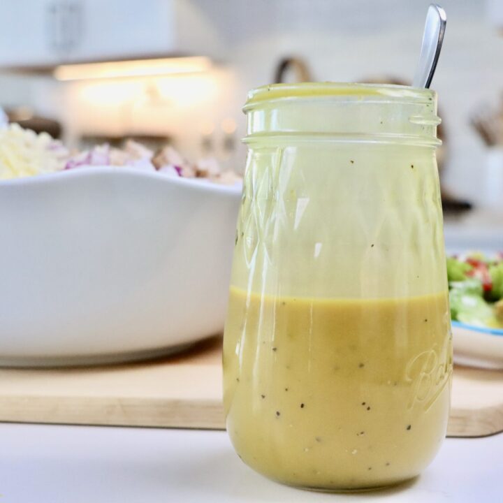Homemade Honey Mustard Dressing in a jar next to a bowl and plate of cobb salad.