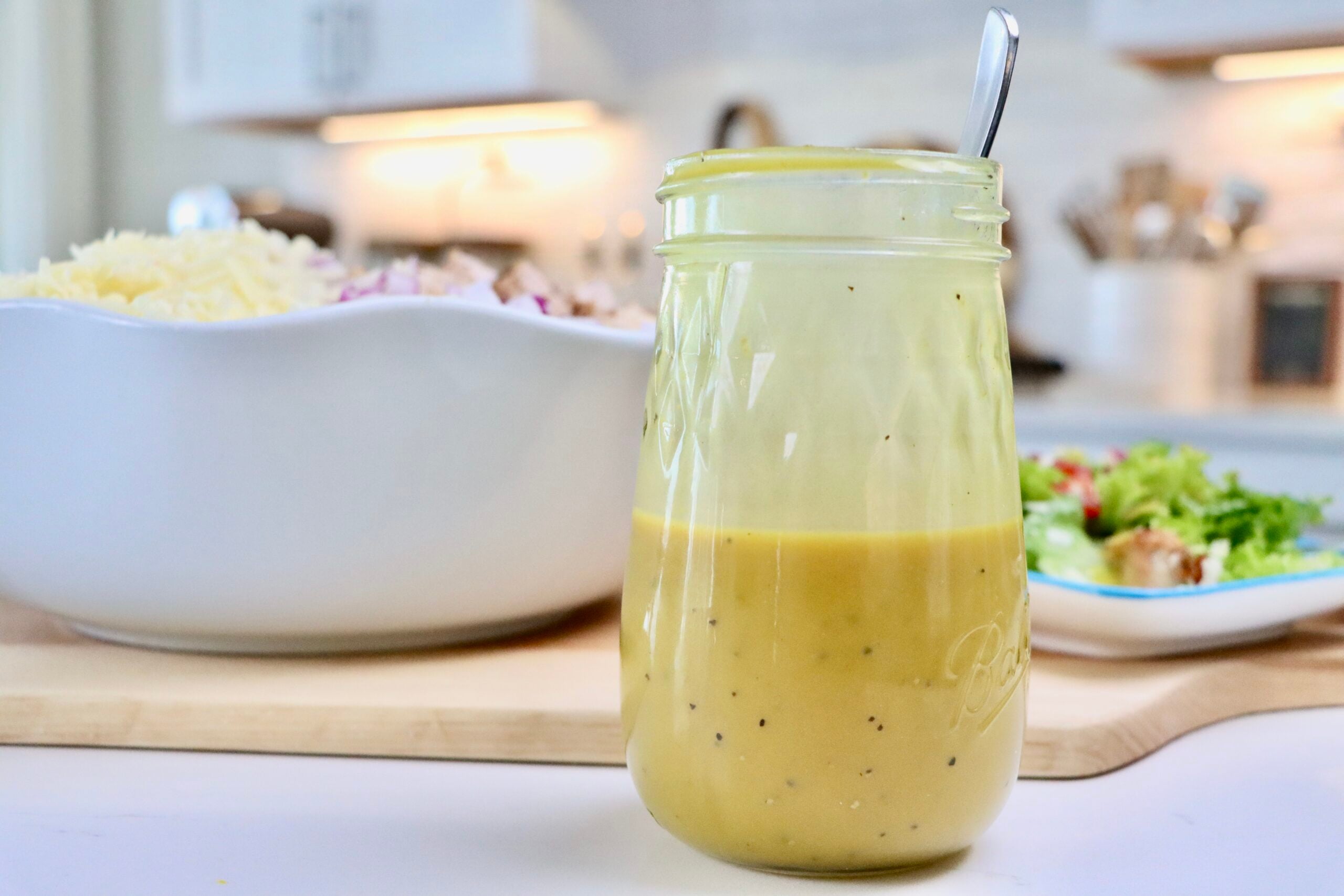 Homemade Honey Mustard Dressing in a jar next to a bowl and plate of cobb salad.