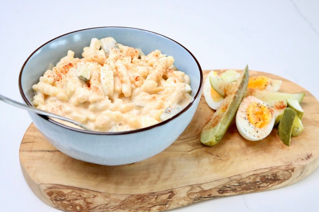 Macaroni Salad on a cutting board with hard boiled eggs and pickles