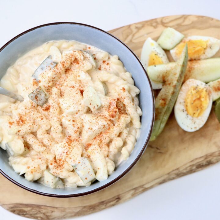 Macaroni Salad on a cutting board with hard boiled eggs and pickles