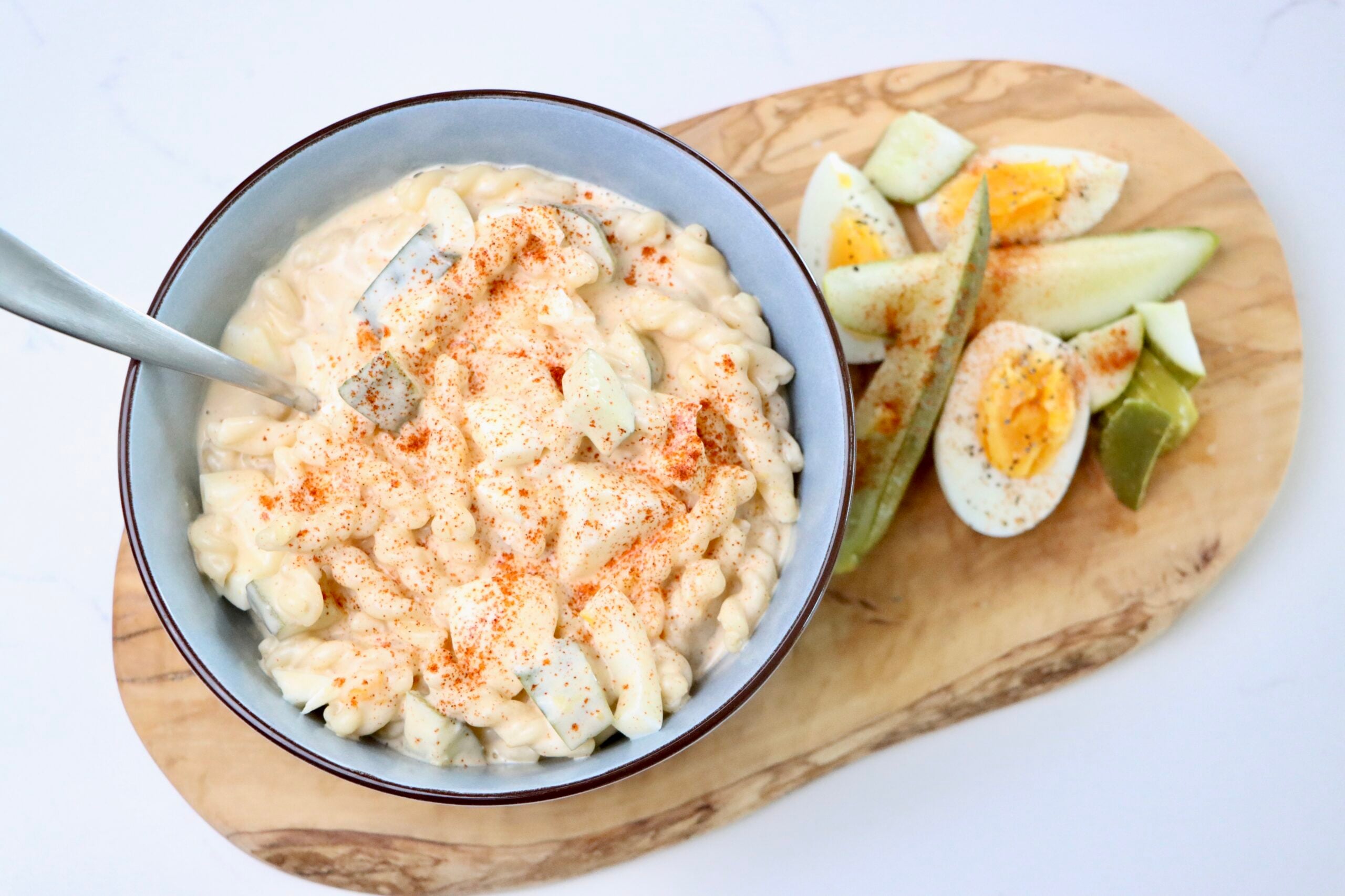 Macaroni Salad on a cutting board with hard boiled eggs and pickles