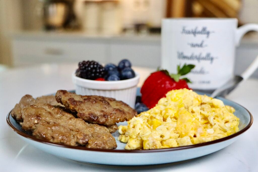 Homemade maple patties on a white plate served with scrambled eggs and a side of mixed berries. A wholesome, from-scratch breakfast using real ingredients.