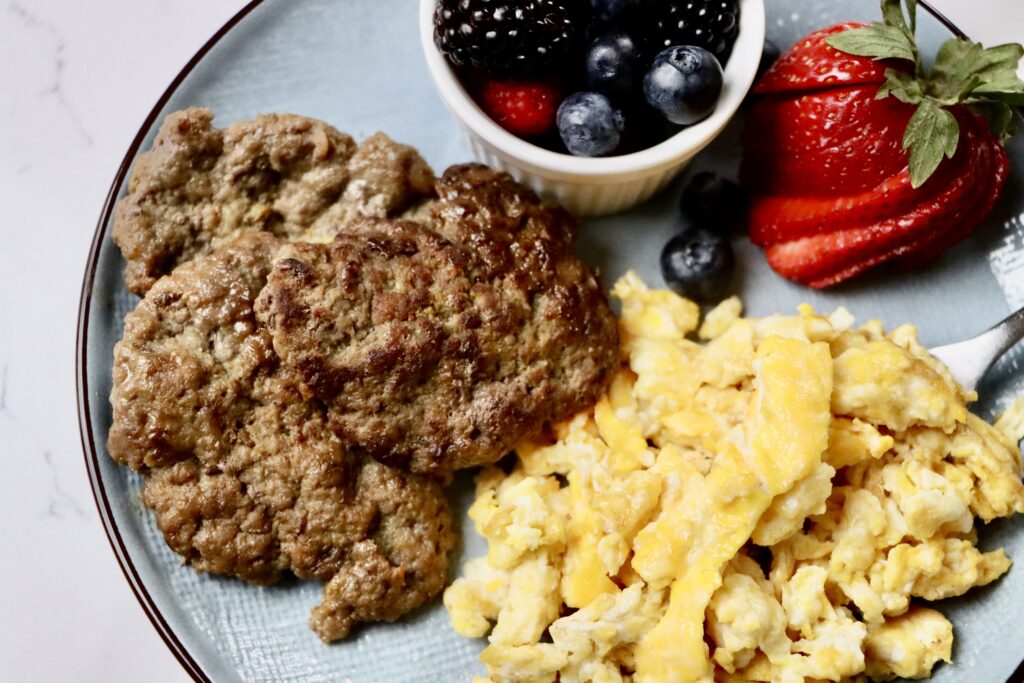 Homemade maple patties on a white plate served with scrambled eggs and a side of mixed berries. A wholesome, from-scratch breakfast using real ingredients.