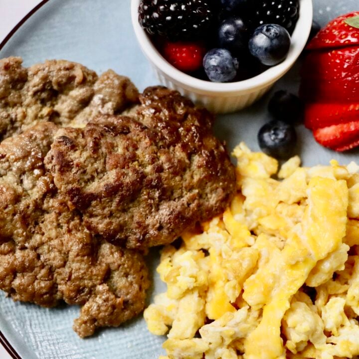 Homemade maple patties on a white plate served with scrambled eggs and a side of mixed berries. A wholesome, from-scratch breakfast using real ingredients.