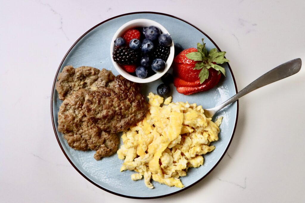 Homemade maple patties on a white plate served with scrambled eggs and a side of mixed berries. A wholesome, from-scratch breakfast using real ingredients.