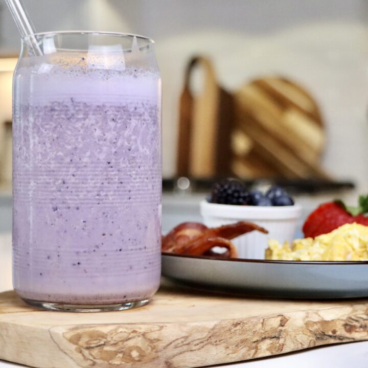 Morning Milkshake served in a glass next to a breakfast plate with scrambled eggs, crispy bacon, and fresh mixed berries on a cutting board.