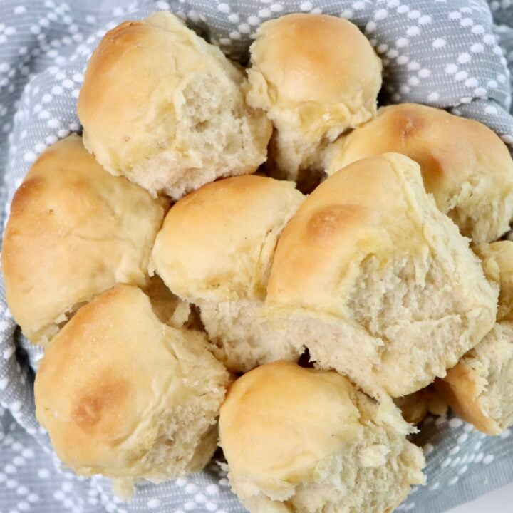 A basket of freshly baked sourdough Hawaiian rolls, golden brown and fluffy, nestled in a gray and white patterned cloth—soft, pull-apart texture perfect for serving at dinner or holiday meals.