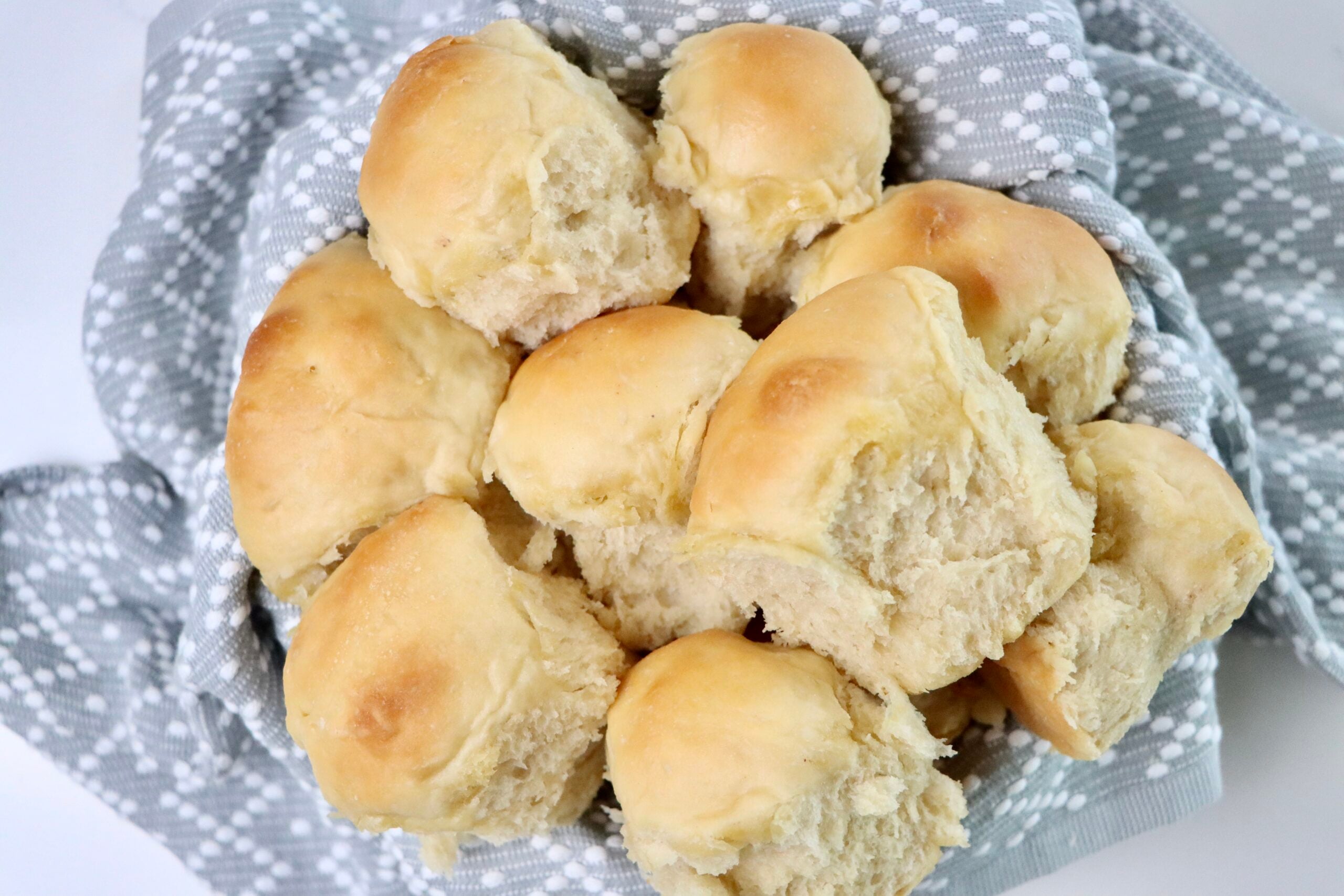 A basket of freshly baked sourdough Hawaiian rolls, golden brown and fluffy, nestled in a gray and white patterned cloth—soft, pull-apart texture perfect for serving at dinner or holiday meals.