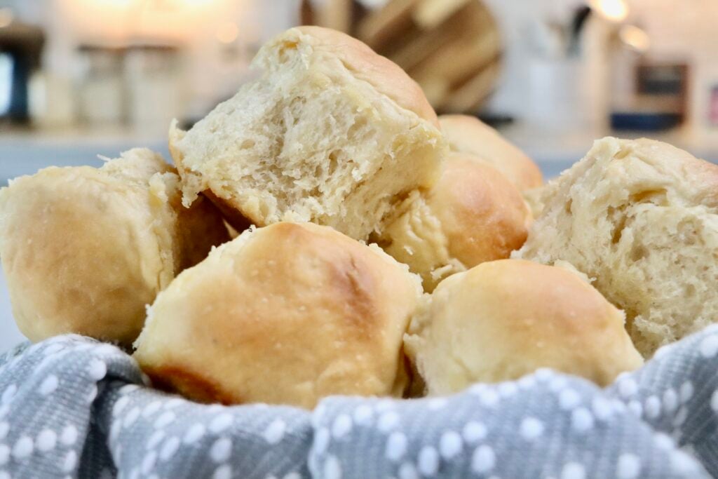 A basket of freshly baked sourdough Hawaiian rolls, golden brown and fluffy, nestled in a gray and white patterned cloth—soft, pull-apart texture perfect for serving at dinner or holiday meals.