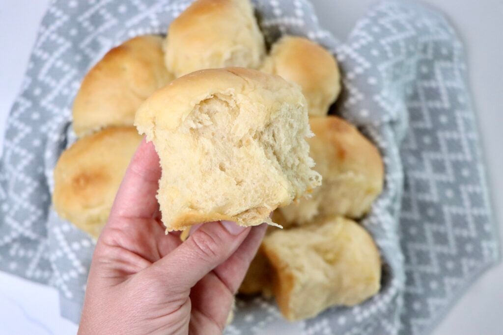 A basket of freshly baked sourdough Hawaiian rolls, golden brown and fluffy, nestled in a gray and white patterned cloth—soft, pull-apart texture perfect for serving at dinner or holiday meals.