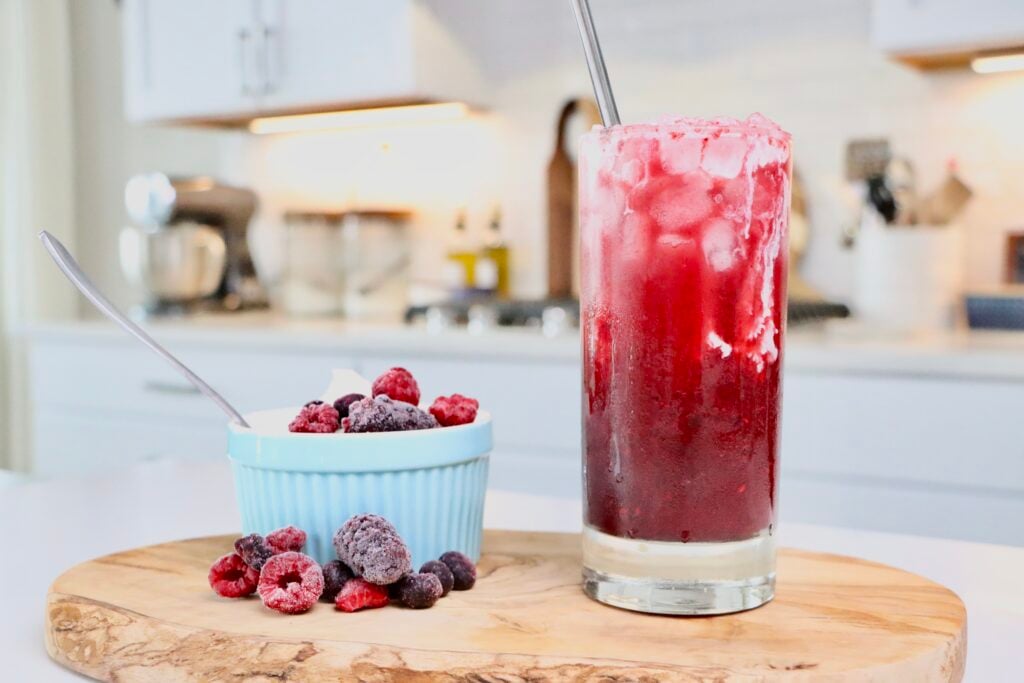 Homemade Cream Soda sitting on a cutting board next to a bowl of homemade whipped cream and berries