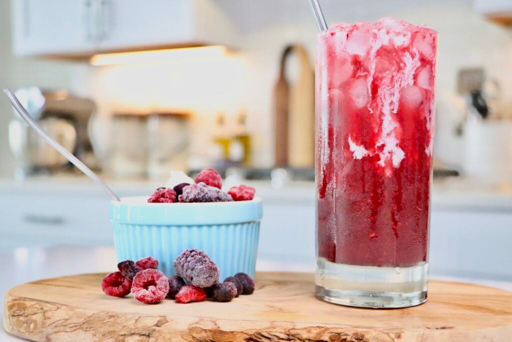 Homemade Cream Soda sitting on a cutting board next to a bowl of homemade whipped cream and berries