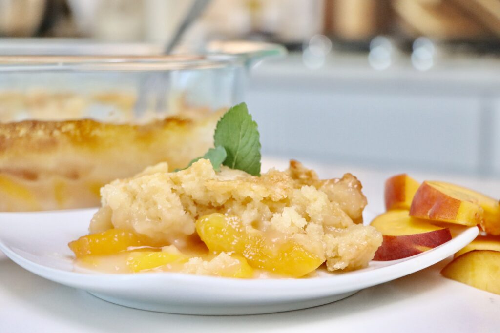 Slice of peach cobbler served on a white plate with vanilla ice cream melting on top