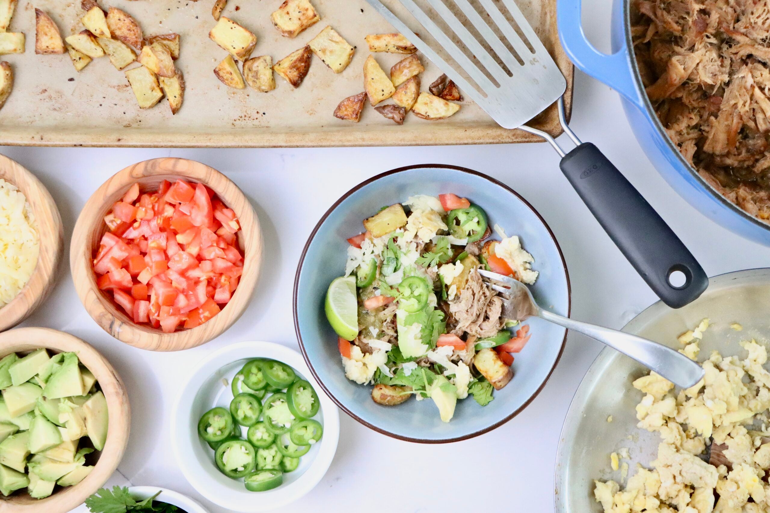 Carnitas Breakfast Bowl with crispy roasted potatoes, scrambled eggs, citrusy pork carnitas, avocado slices, shredded cheddar, salsa verde, and fresh cilantro in a bowl.