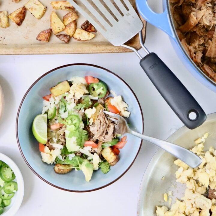 Carnitas Breakfast Bowl with crispy roasted potatoes, scrambled eggs, citrusy pork carnitas, avocado slices, shredded cheddar, salsa verde, and fresh cilantro in a bowl.