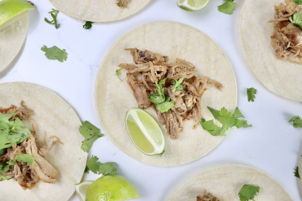 Citrusy carnitas served in soft corn tortillas with fresh cilantro and lime wedges, juicy pork shoulder shredded and topped with orange and lime zest.
