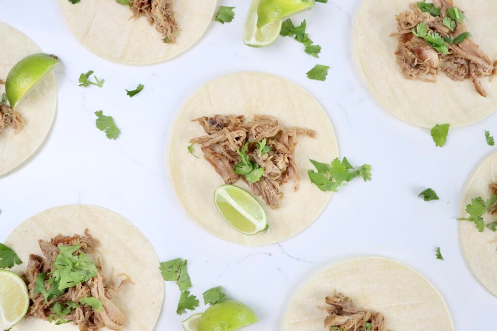 Citrusy carnitas served in soft corn tortillas with fresh cilantro and lime wedges, juicy pork shoulder shredded and topped with orange and lime zest.