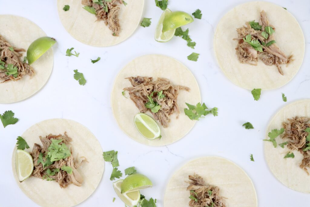 Citrusy carnitas served in soft corn tortillas with fresh cilantro and lime wedges, juicy pork shoulder shredded and topped with orange and lime zest.