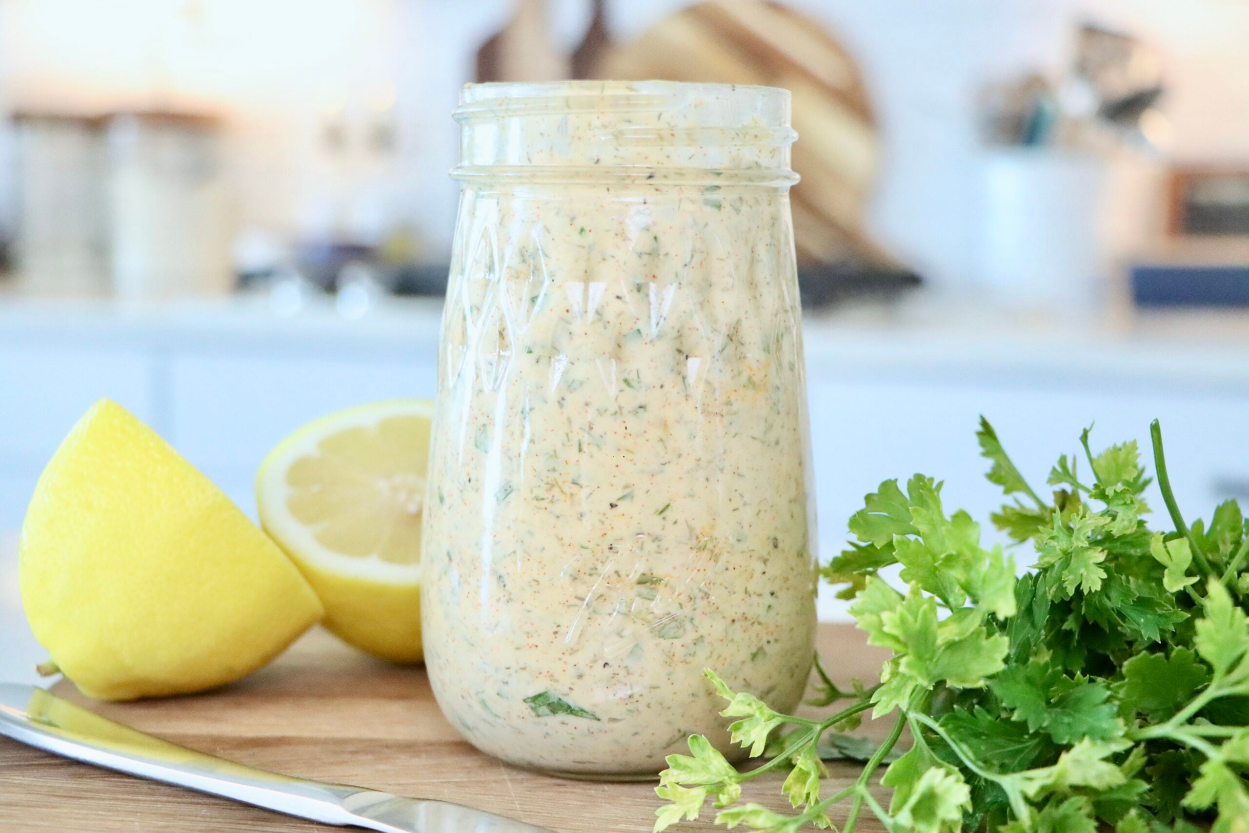 Herb Mayo in a glass jar on a cutting board next to a cut lemon and fresh parsley